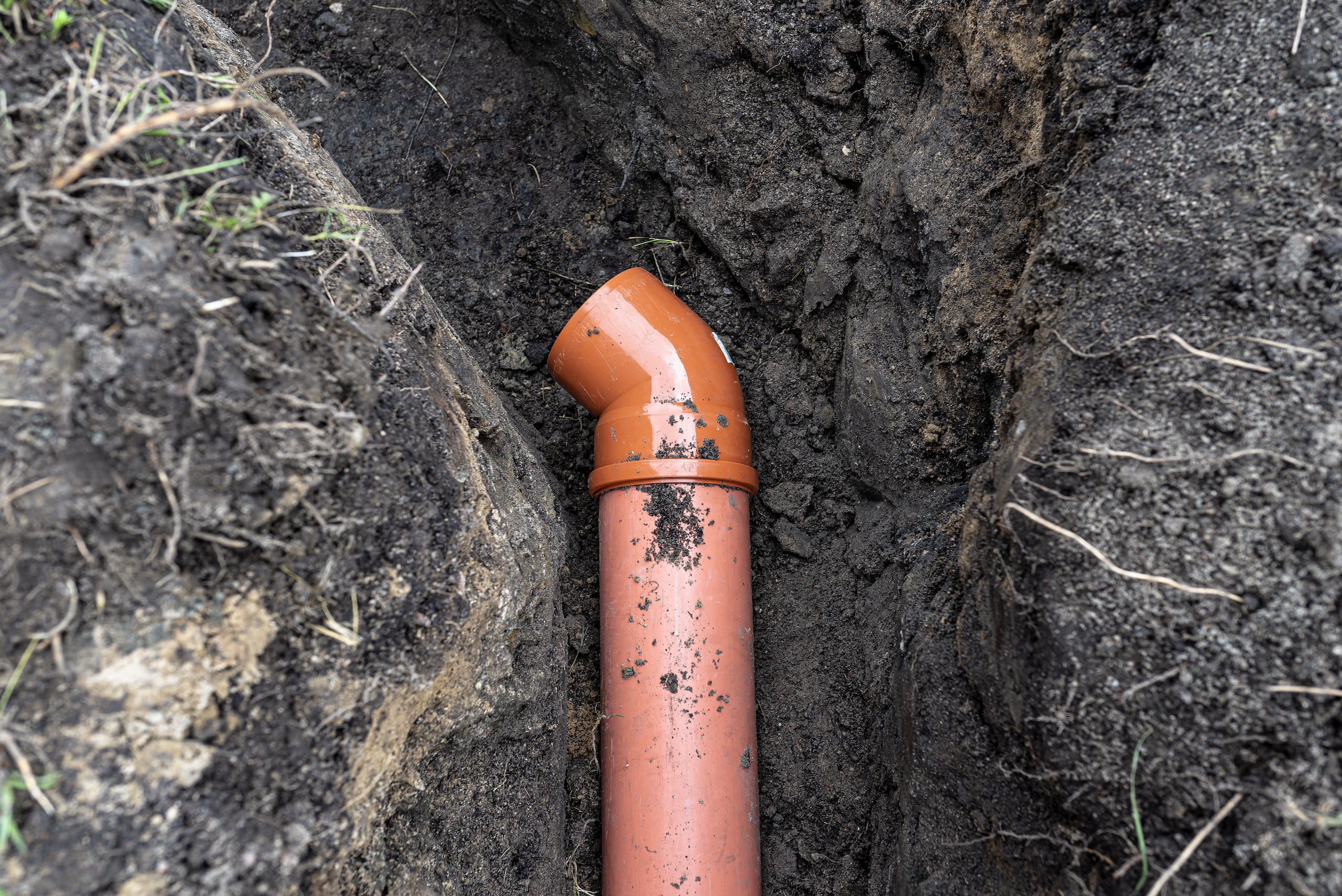 An orange plastic pipe from a septic tank with a diameter of 160 mm lying in a ditch.